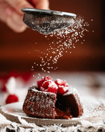 lava-cakes-dark-chocolate-raspberry A Lava Cake filled with liquid chocolate and topped with raspberries is sprinkled with icing sugar.