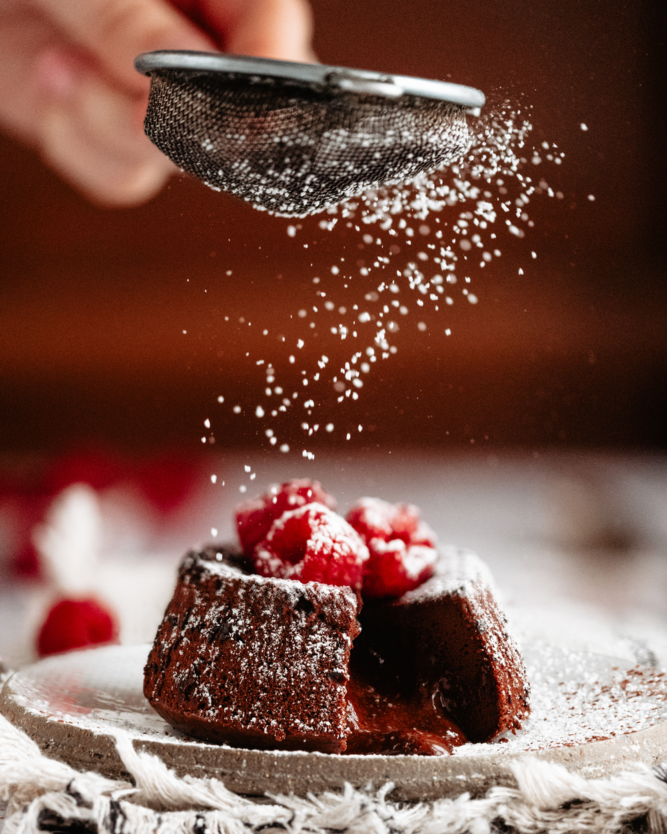 A Lava Cake filled with liquid chocolate and topped with raspberries is sprinkled with icing sugar.