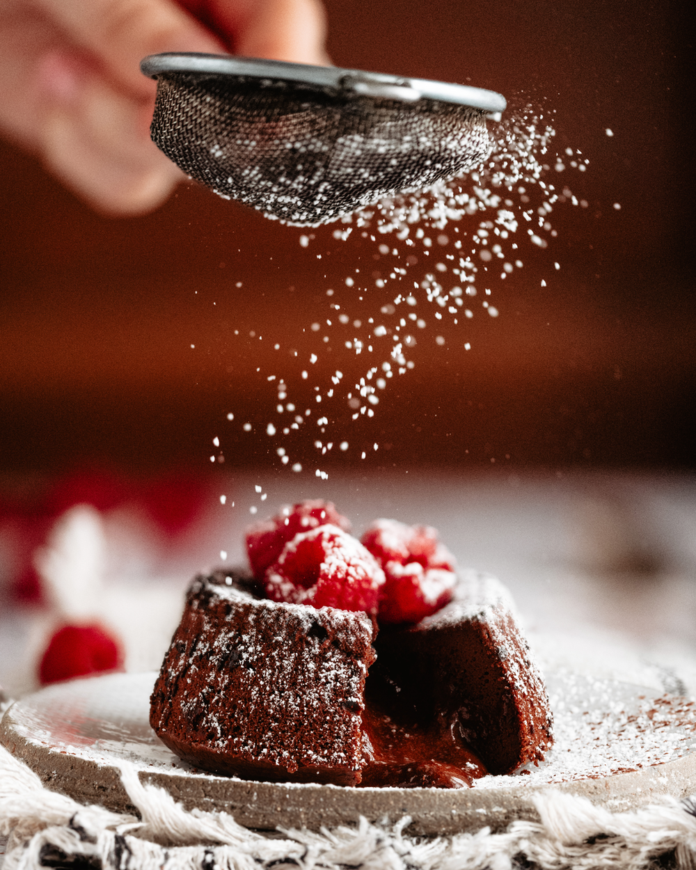 A Lava Cake filled with liquid chocolate and topped with raspberries is sprinkled with icing sugar.