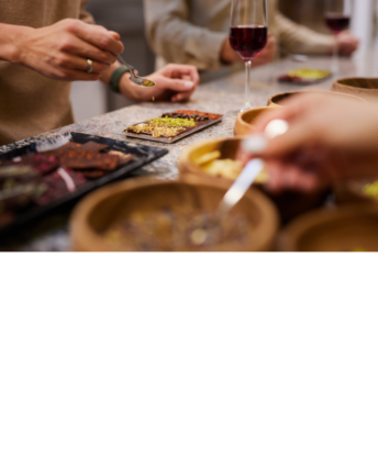 workshop-restaurant-vossini-schokoladenhotel-westerstede Frauenhände, die an einem Tisch mit Weingläsern Schokoladentafeln mit Zutaten bestreuen.