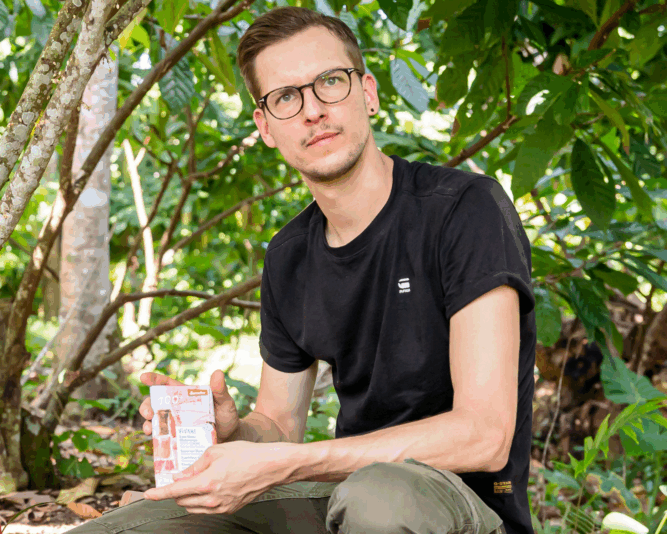 gerrit-wiezoreck-geschäftsführer-vivani-bioschokolade Gerrit Wiezoreck - Geschäftsführer von VIVANI - sitzt im Kakaowald und hält eine Tafel Demeter-Bioschokolade in der Hand.