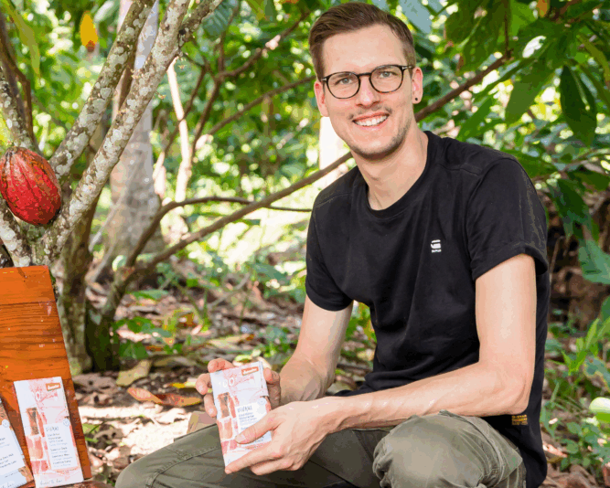 Gerrit Wiezoreck, managing director of VIVANI organic chocolate, with a chocolate bar in front of cocoa trees.