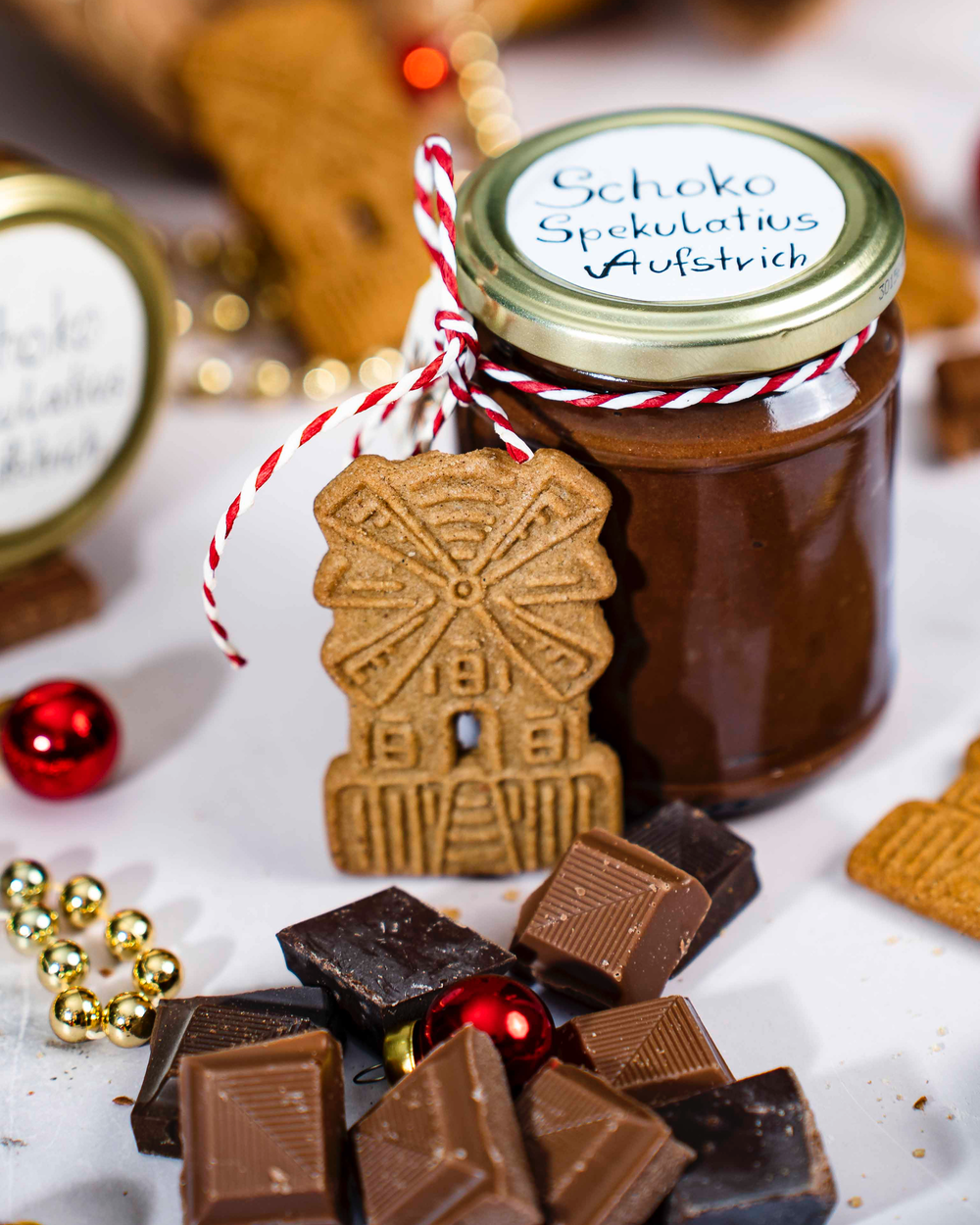 Ein Glas Schoko-Spekulatius-Aufstrich mit Schokoladenstückchen, Gewürzspekulatius und Weihnachtsdekoration.