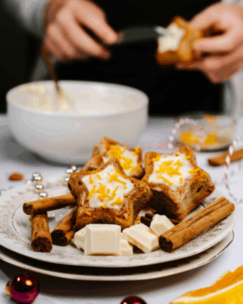 Zimtsternküchlein mit weißer Schokoladenglasur auf einem Teller mit Zimtstangen und weißen Schokoladenstückchen.