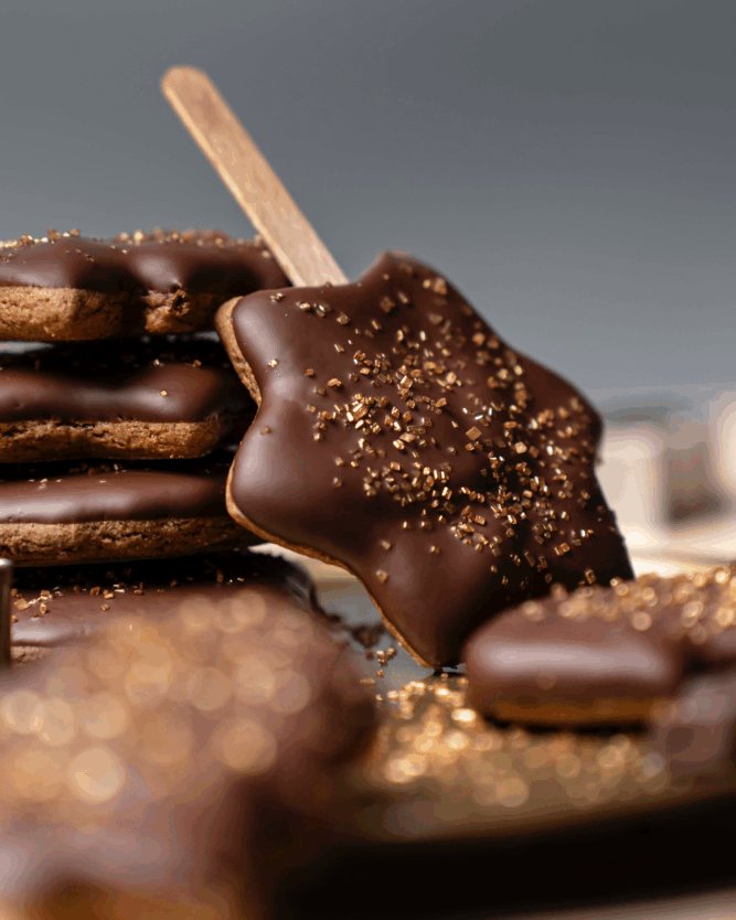 Schokolierte Lebkuchen am Stiel mit goldenem Streuseldekor.