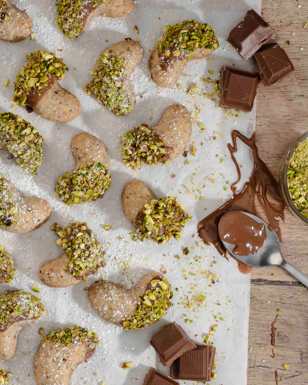 Vanillekipferl mit geschmolzener Vollmilchschokolade und aufgestreuten, gehackten Pistazien.