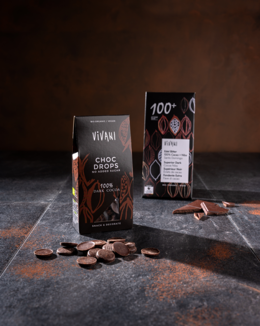 Die VIVANI Choc Drops im Vordergrund, dahinter die Schokoladentafel Edel Bitter 100 % Cacao + Nibs.