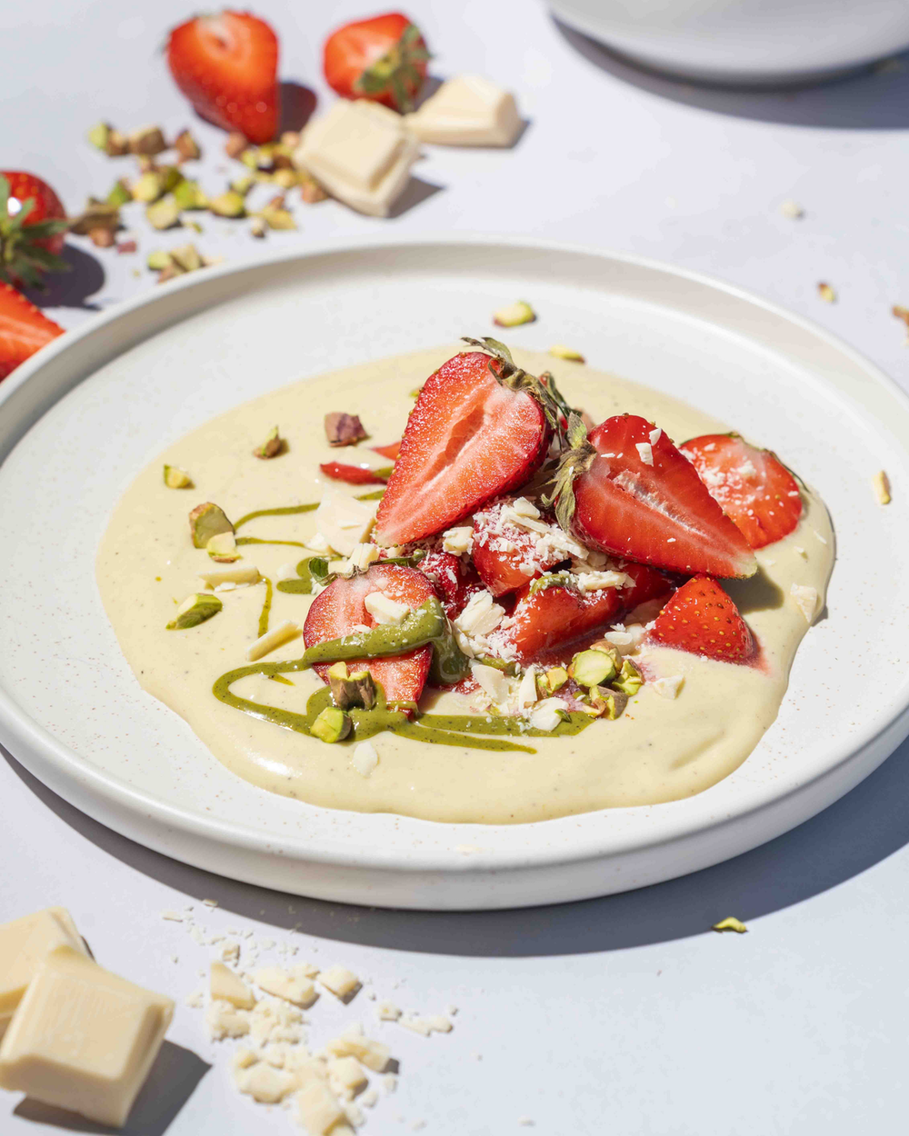 Ein Dessert aus weißer Schoko-Pistaziencreme, angerichtet mit Erdbeeren und grünem Pistazienmus.