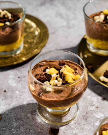 Mehrere Dessertgläser geschichtet mit Schokoladenmousse, frischen Mangostückchen und Schokoladendekoration.