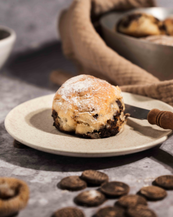 choc-drops-broetchen-vivani Ein Schokobrötchen mit einem Messer auf einem Teller angerichtet, drumherum verteilt einige VIVANI Choc Drops.