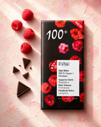 edel-bitter-100-prozent-cacao-plus-himbeer-vivani-bio-schokolade Die Tafel 100 % Cocoa + Himbeer von VIVANI Bio-Schokolade, mit frischen Himbeeren und Schokoladenstückchen daneben.