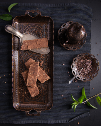 schokoladenhalva-vivani-bio-schokolade Mehrere Scheiben Schokoladenhalva auf einer Platte angerichtet mit orientalischer angehauchter Dekoration, Kakaonibs und Minzblättern.