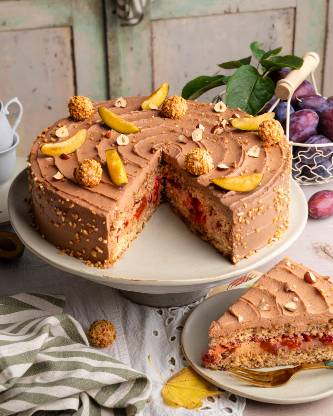 Eine angeschnittene Nougattorte mit Pflaumenschicht, dekorativ auf einem Tisch angerichtet.