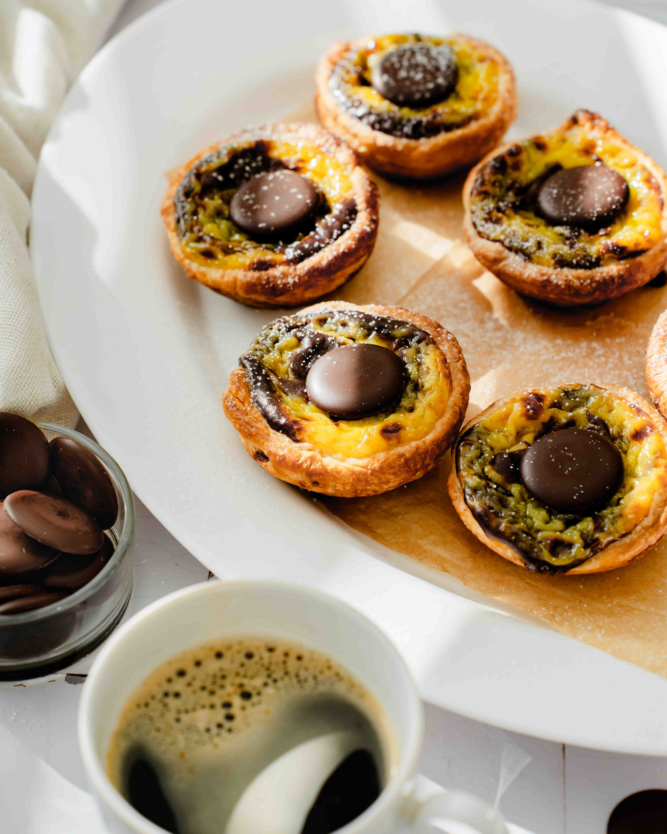 Ein Teller mit mehreren Pastéis de Nata mit marmorierter Creme und einem Schokoladenplättchen.